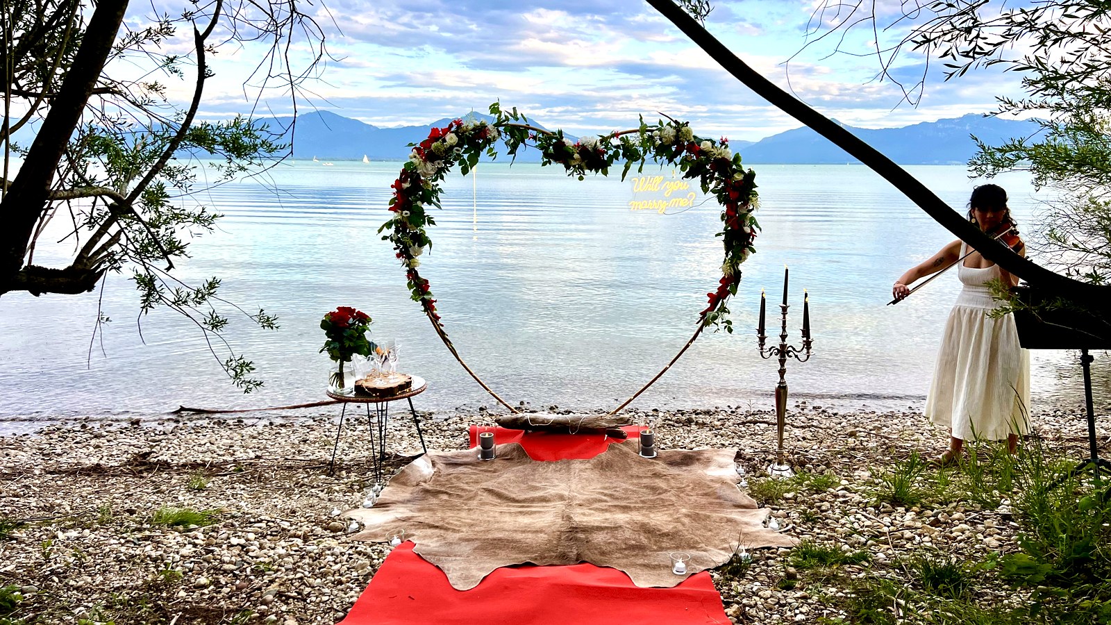 Blumenherz mit Will-you-marry-me-Schriftzug und Geigerin am Chiemseeufer beim Heiratsantrag von Zoi und Ramazan