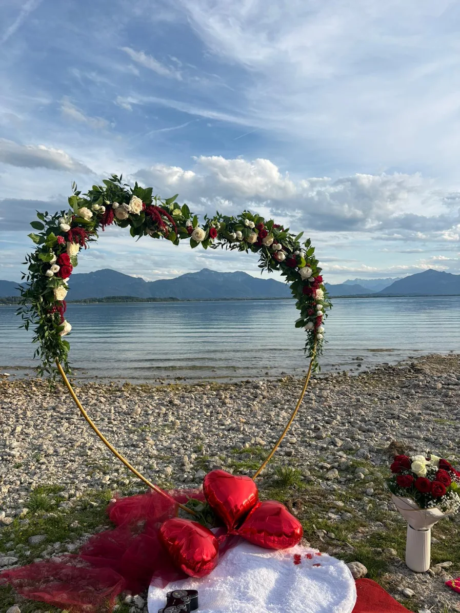 Herzförmiger Blumenbogen am Chiemseeufer mit roten Herzballons beim Heiratsantrag von Saša